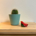 Small ceramic sculpture of a red bird, sitting next to a potted cactus.
