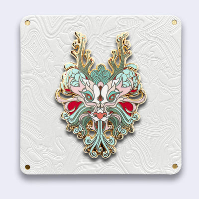 Elaborately designed enamel pin of a mint green and light red dragon head, with gold outlines. It has many floral elements with mum like ears and branches for antlers.
