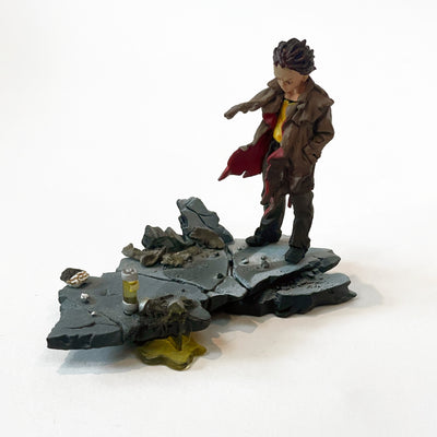 Vinyl figure of a boy with spiky hair standing on a segment of a concrete platform, with many rock chunks on it and a chemical colored liquid leaking. They stand wearing a tattered jacket, with their hands in their pockets and the wind blowing.