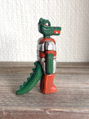 Whittled wooden sculpture of a green dinosaur, akin to a crocodile, wearing a space suit of silver and red.