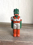 Whittled wooden sculpture of a green dinosaur, akin to a crocodile, wearing a space suit of silver and red.