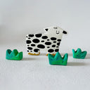 Clay sculpture of a stylistic cow, with a pointed head and a very simple smiley face. 3 sculpted clumps of grass surround it.