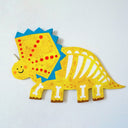 A colorful wooden dinosaur skeleton wall decor piece featuring a yellow body, blue spikes, red spots, and white bones, shown against a white textured wall.