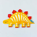 A colorful flat dinosaur wall art piece shaped like a stegosaurus, featuring a yellow body, red plates, white bones, and a small blue tail, displayed on a light textured wall.