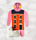 Paper cut out of a person wearing a dress that resembles a building. Sitting at her feet is a fluffy white dog.