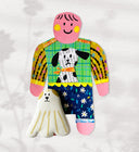 Paper cut out of a person wearing a shirt with patterning and a dog on it. Sitting at her feet is a long haired white dog.
