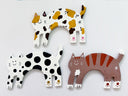 Three clay cat-shaped sculptures, laying flat, with different color patterns on a white background