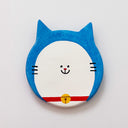 Round clay sculpture of a cat face, totally flat, with blue and white coloring and a red collar with a gold bell. It has a tiny smile in the middle of the face.