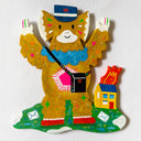 Flat colorful sculpture of a kaiju monster, a cute brown character dressed like a mailman with a hat and sling bag, standing in front of a tiny house on fire with letters on the ground.