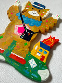Flat colorful sculpture of a kaiju monster, a cute brown character dressed like a mailman with a hat and sling bag, standing in front of a tiny house on fire with letters on the ground.