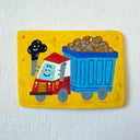 A colorful hand-painted flat artwork featuring a cartoon dump truck on a bright yellow background, mounted on a textured white wall.