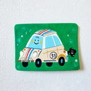 A flat artwork featuring a cartoon race car and a small black dog on a green background, mounted on a white textured wall.