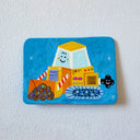 A flat artwork featuring a colorful, whimsical painting of a yellow bulldozer on a bright blue background, mounted on a textured white wall.