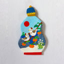 A hand-painted clay wall hanging shaped like a snuff bottle, featuring two birds, orange persimmons, white flowers, and a red sun on a light blue background, mounted on a textured white wall.