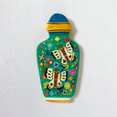 A hand-painted clay wall vase with a green body decorated with colorful butterflies, flowers, and leaves, topped with a blue and yellow lid, mounted on a textured white wall.