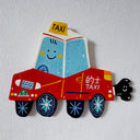 Flat sculpture of a cartoon style taxi red in coloring with a cute smiley face and a cartoon plume of exhaust smoke coming out the tailpipe.