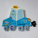 Flat sculpture of a cartoon style taxi, blue in coloring with a cute smiley face and a cartoon plume of exhaust smoke coming out the tailpipe.