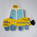 Flat sculpture of a cartoon style taxi, yellow in coloring with a cute smiley face and a cartoon plume of exhaust smoke coming out the tailpipe.