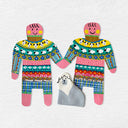 2 paper cut out dolls, wearing patterned sweaters and holding hands. A small clay dog sits in between them.
