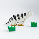 A stylized white dinosaur sculpture with black stripes, a smiling face, and yellow feet, shown on a light gray background with two small green plant shapes.