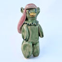 Ceramic sculpture of a green fish creature - Japanese yokai Amabie - standing on thick legs with her arms at her side. She has long pink hair and a bird/turtle beak. 