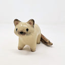 Ceramic sculpture of a tan cat with dark brown ears, paws, tail and snout. It stands with black eyes and a simply drawn nose and whiskers. It has 2 tails.