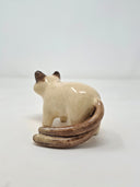 Ceramic sculpture of a tan cat with dark brown ears, paws, tail and snout. It stands with black eyes and a simply drawn nose and whiskers. It has 2 tails.