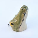 Ceramic sculpture of a crocodile head, yellowish green with a cream colored underside. At the top of its head is a wire hanging hardware.