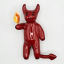 Ceramic sculpture of a red, devil creature with a flame coming out its hand.