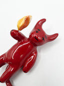 Ceramic sculpture of a red, devil creature with a flame coming out its hand.