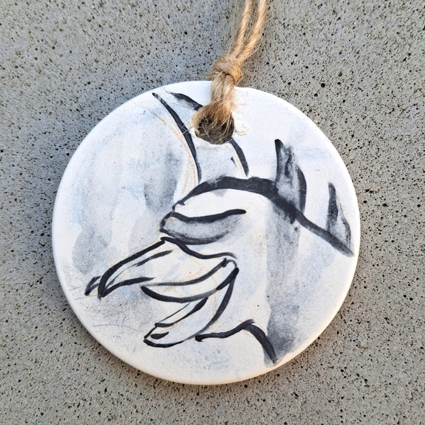 Round ceramic ornament with a black and white design of the kaiju Gigan hanging from brown twine.