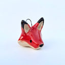 Ceramic sculpture of a red fox's head, with black tipped ears and a cream underside of its fur. It has a semicircle wire hanging attachment atop it.
