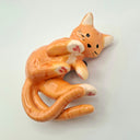 Ceramic orange cat figurine with 2 tails, laying on its side on a light gray background