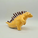 Ceramic sculpture of a orange-ish tan kaiju dinosaur creature with many thin spikes on its back, akin to a porcupine. Spikes look like they are chocolate dipped.
