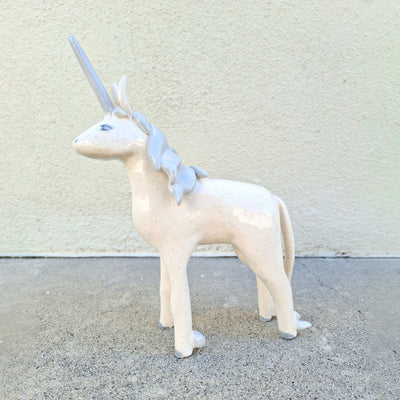 Unicorn ceramic sculpture with a light gray horn and mane on a concrete surface.