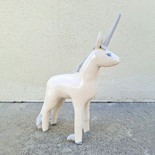 Unicorn ceramic figurine on a concrete surface with a light gray background