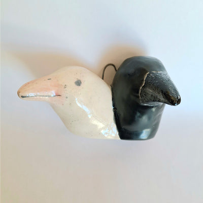 Two ceramic crow figures, heads only, both growing out of the same neck - one beige and one black, on a light background