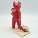 Red ceramic sculpture of a devil character, standing with guinea pigs.