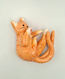 Ceramic orange cat figurine with 2 tails, laying on its side on a light gray background