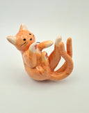 Ceramic orange cat figurine with 2 tails, laying on its side on a light gray background