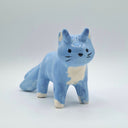 A small blue cat figurine with white chest, paws, and ears, standing on a light gray background.