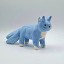 A small ceramic horned cat figurine in light blue with white accents on its chest, paws, and tail tips, standing on a light gray background.