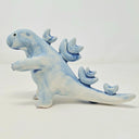 Ceramic sculpture of a Godzilla like kaiju, with rounded edges for its head and arms. Its spikes are rounder, more flower-like shapes.