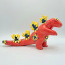 Red ceramic figurine of a kaiju monster akin to a dinosaur, with a very long tail and spikes down its back with floral patterns on a white background