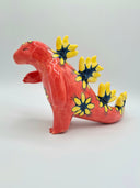 Red ceramic figurine of a kaiju monster akin to a dinosaur, with a very long tail and spikes down its back with floral patterns on a white background
