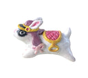 Decorative figurine of a white bunny positioned like a mount - with a qulited pink and gold saddle and a fance gold and purple hat. 