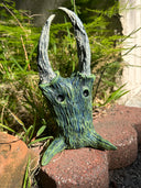 Green dragon head sculpture on a natural background with plants and stones.