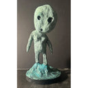 Paper clay sculpture of a green alien like creature - a version of a Kodama - standing on a rocky base.
