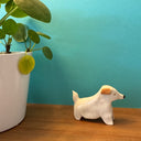 Ceramic sculpture of a small, white dog with longer fur and a floppy brown ear.