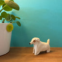 Ceramic sculpture of a small, white dog with longer fur and a brown circle around its eye.